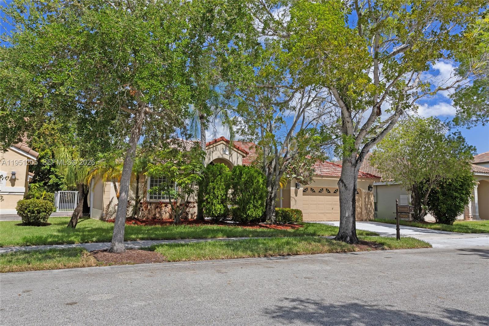 A single-story house with a tan stucco exterior, tile roof, and mature trees in front — 798 Verona Lake Dr, Weston FL 33326, WESTON, FL