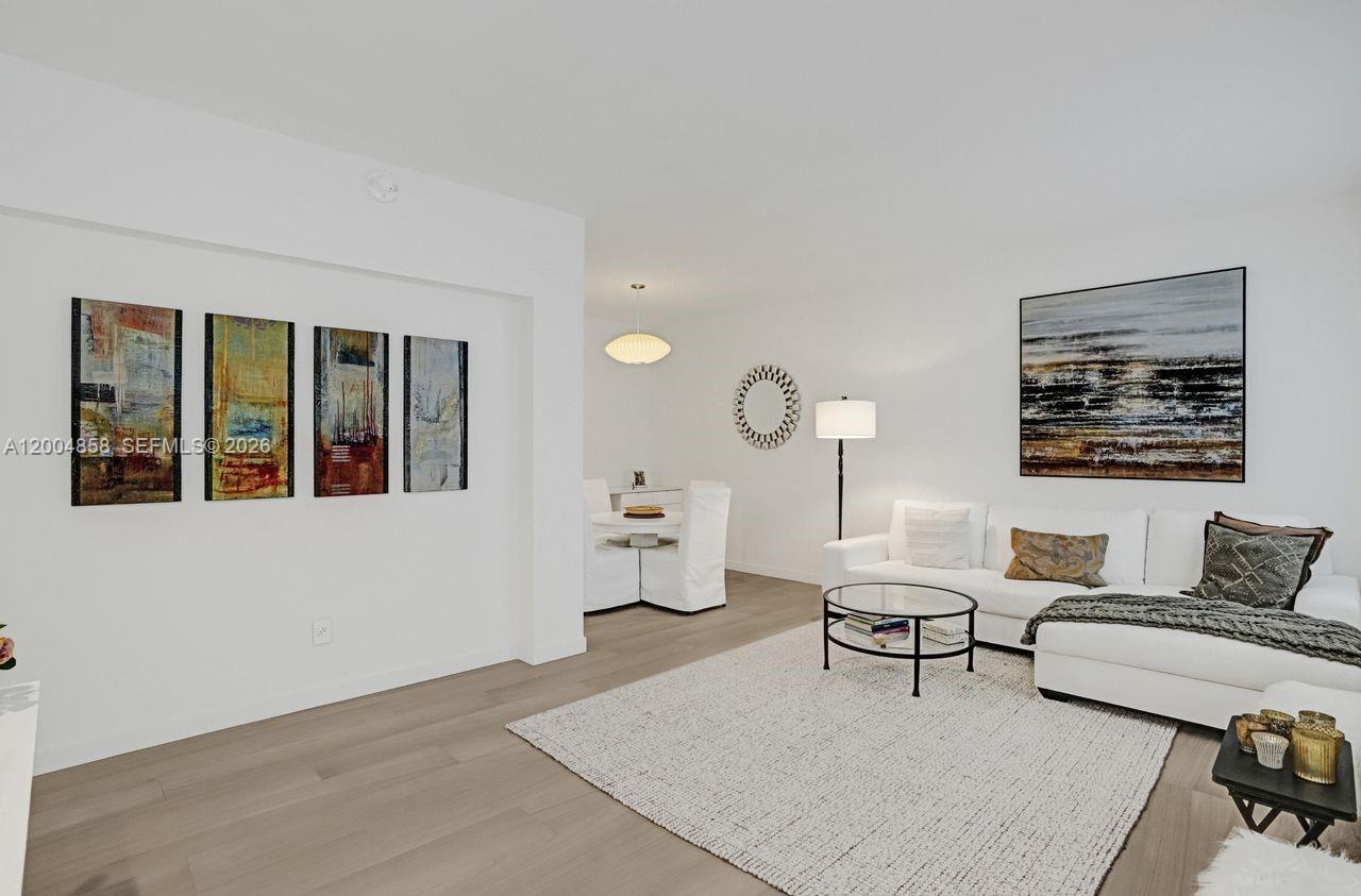 A living room features white walls, light wood flooring, a white sectional sofa, and artwork — 625 Biltmore Way # 103, Coral Gables FL 33134, CORAL GABLES, FL