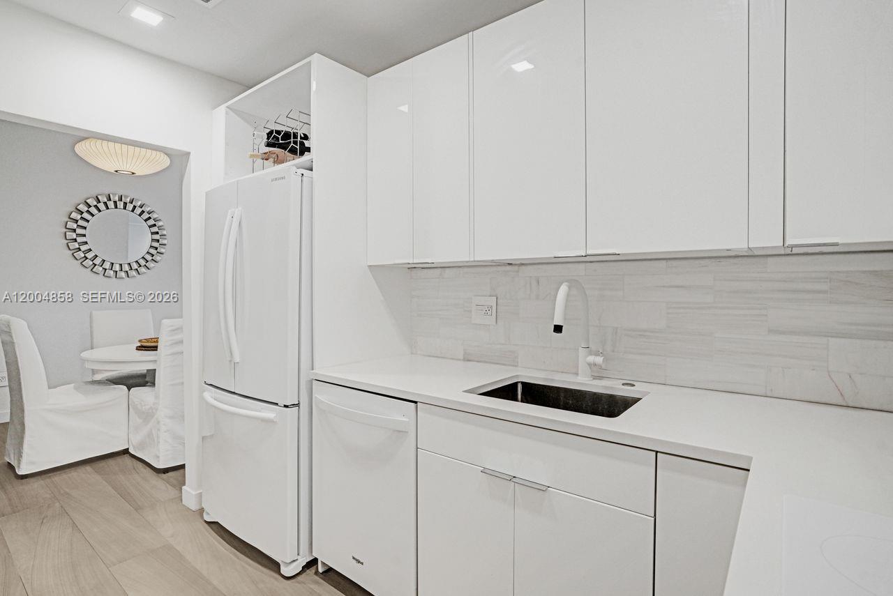 A modern kitchen features white cabinetry, a stainless steel sink, and a white refrigerator — 625 Biltmore Way # 103, Coral Gables FL 33134, CORAL GABLES, FL