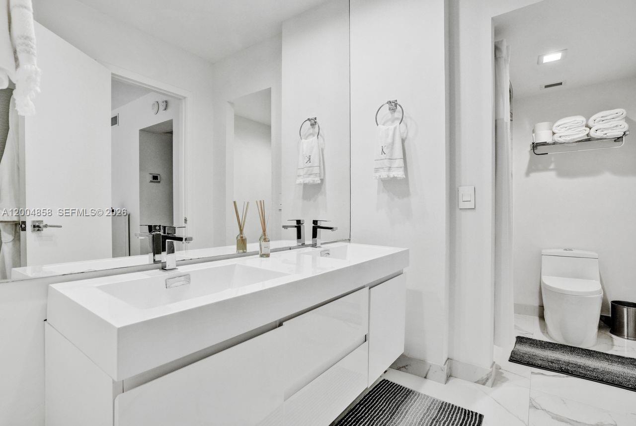 A modern white bathroom features a double vanity with a large mirror and marble flooring — 625 Biltmore Way # 103, Coral Gables FL 33134, CORAL GABLES, FL