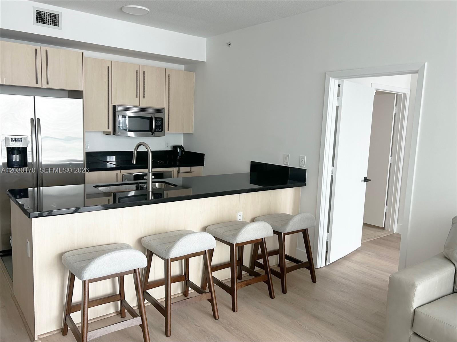A kitchen features light wood cabinets, black countertops, a breakfast bar with four stools, and stainless appliances — 79 SW 12th St, Miami FL 33130, MIAMI, FL