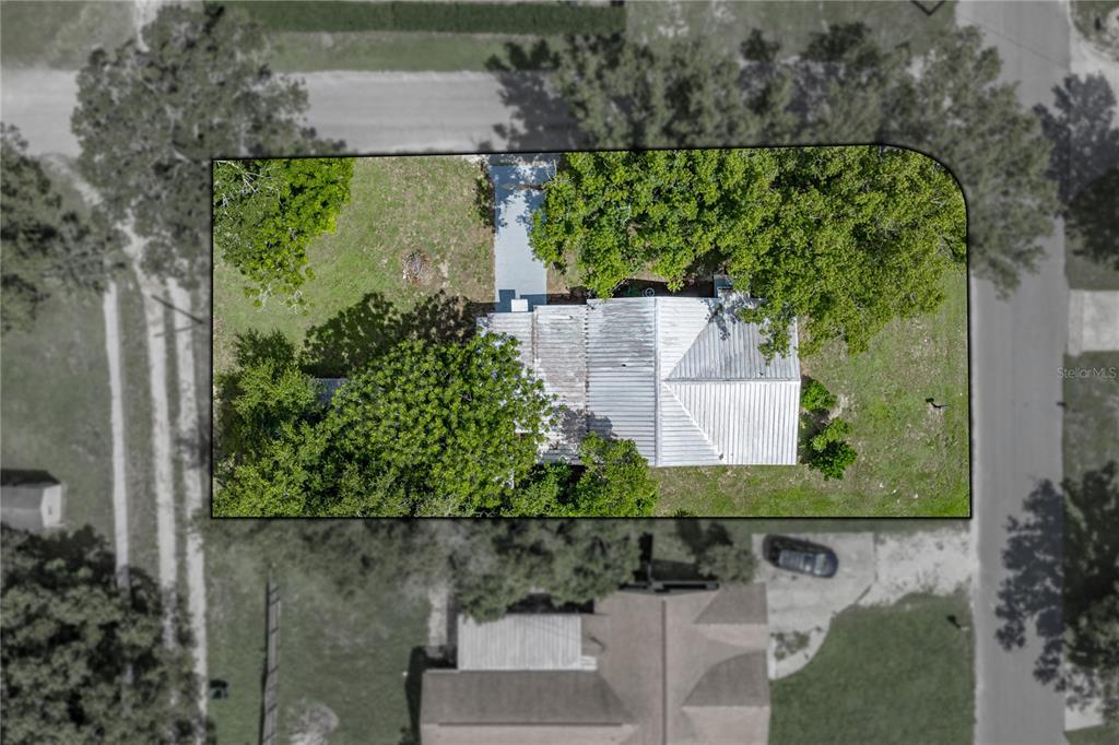 An aerial view shows a house with a metal roof surrounded by trees and grass — 5207 10TH STREET, ZEPHYRHILLS, FL