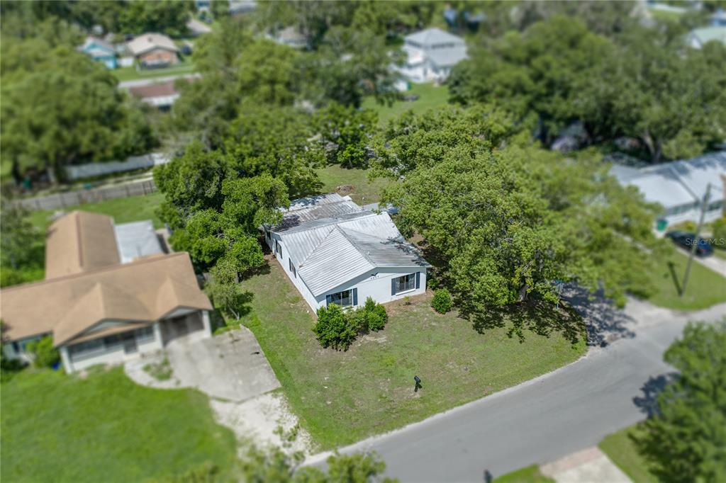 An aerial view shows a white house with a metal roof surrounded by trees — 5207 10TH STREET, ZEPHYRHILLS, FL
