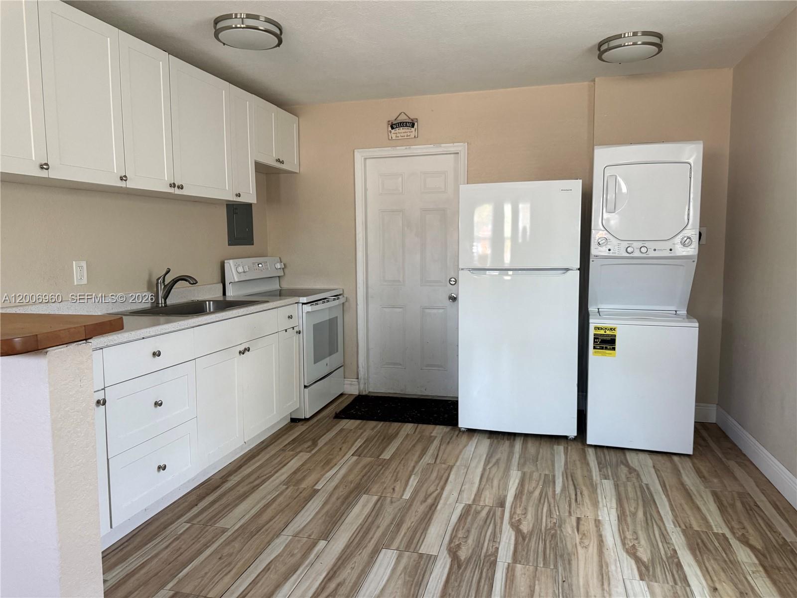 A kitchen features white cabinets, a stove, a refrigerator, and a stacked washer-dryer unit — 508 Beech Rd, West Palm Beach FL 33409, WEST PALM BEACH, FL