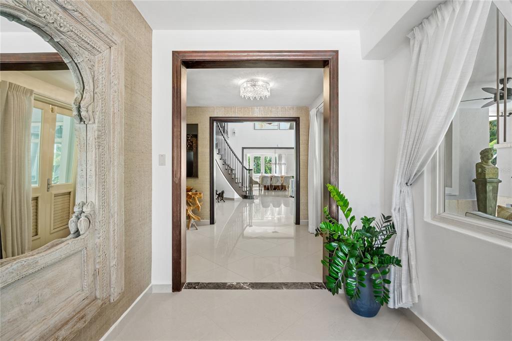 A view through a wooden doorway into a tiled foyer with a staircase and chandelier — 446 DORADO BEACH EAST, DORADO, PR