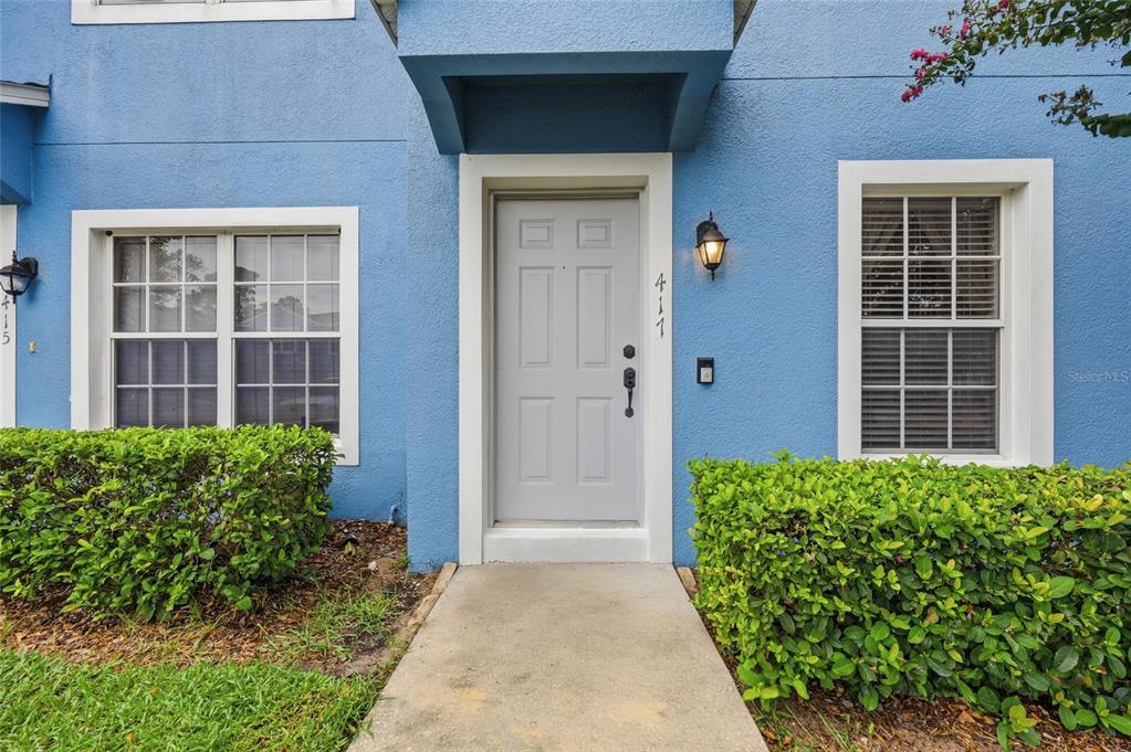 A blue exterior wall features a gray front door, two windows, and green landscaping — 417 WILTON CIRCLE, SANFORD, FL