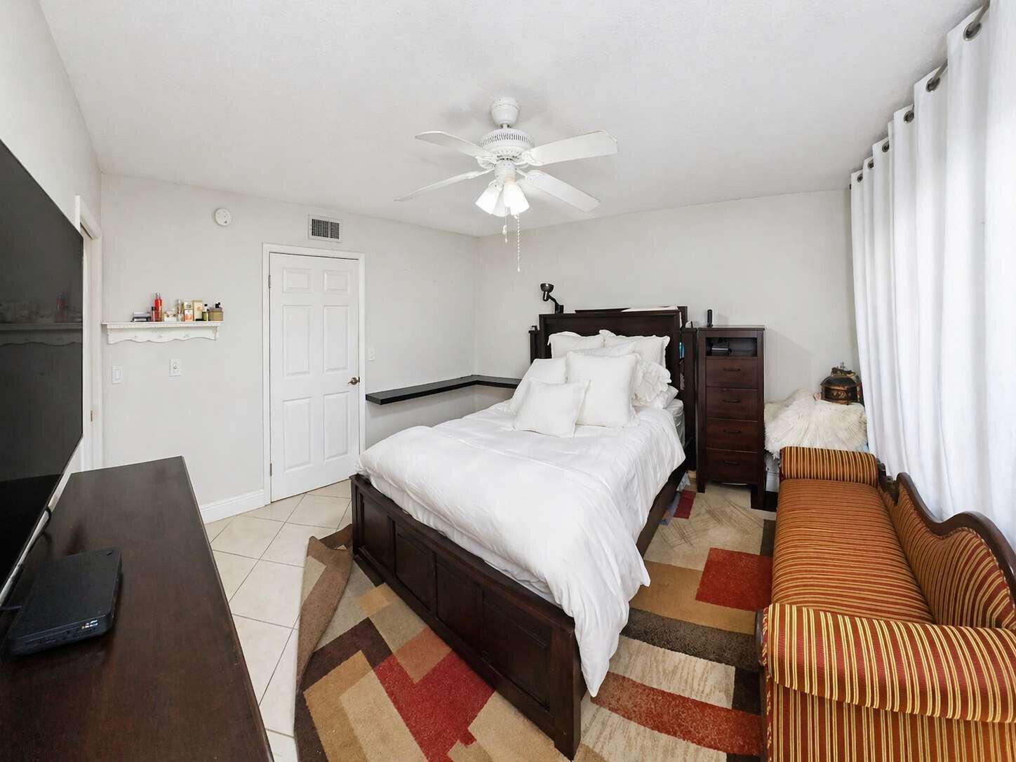 A bedroom features a dark wood bed, a striped bench, and a large television — 5160 Las Verdes Circle # 103, Delray Beach FL 33484, DELRAY BEACH, FL