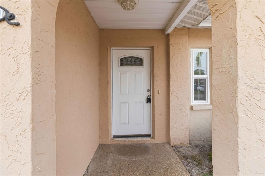 A white front door is centered in a covered entryway with tan stucco walls — 16329 CARIBBEAN COURT, HUDSON, FL