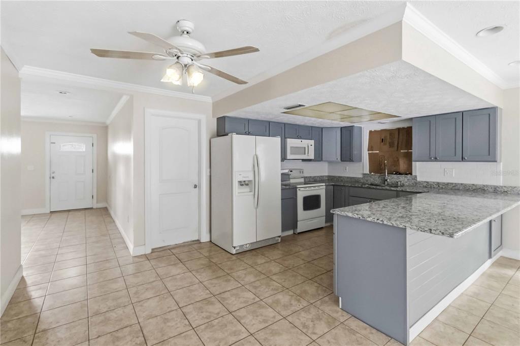 A kitchen features gray cabinets, granite countertops, white appliances, and light-colored tile flooring — 16329 CARIBBEAN COURT, HUDSON, FL