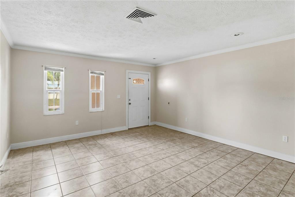 An empty room features beige walls, tile flooring, two windows, and a white front door — 16329 CARIBBEAN COURT, HUDSON, FL