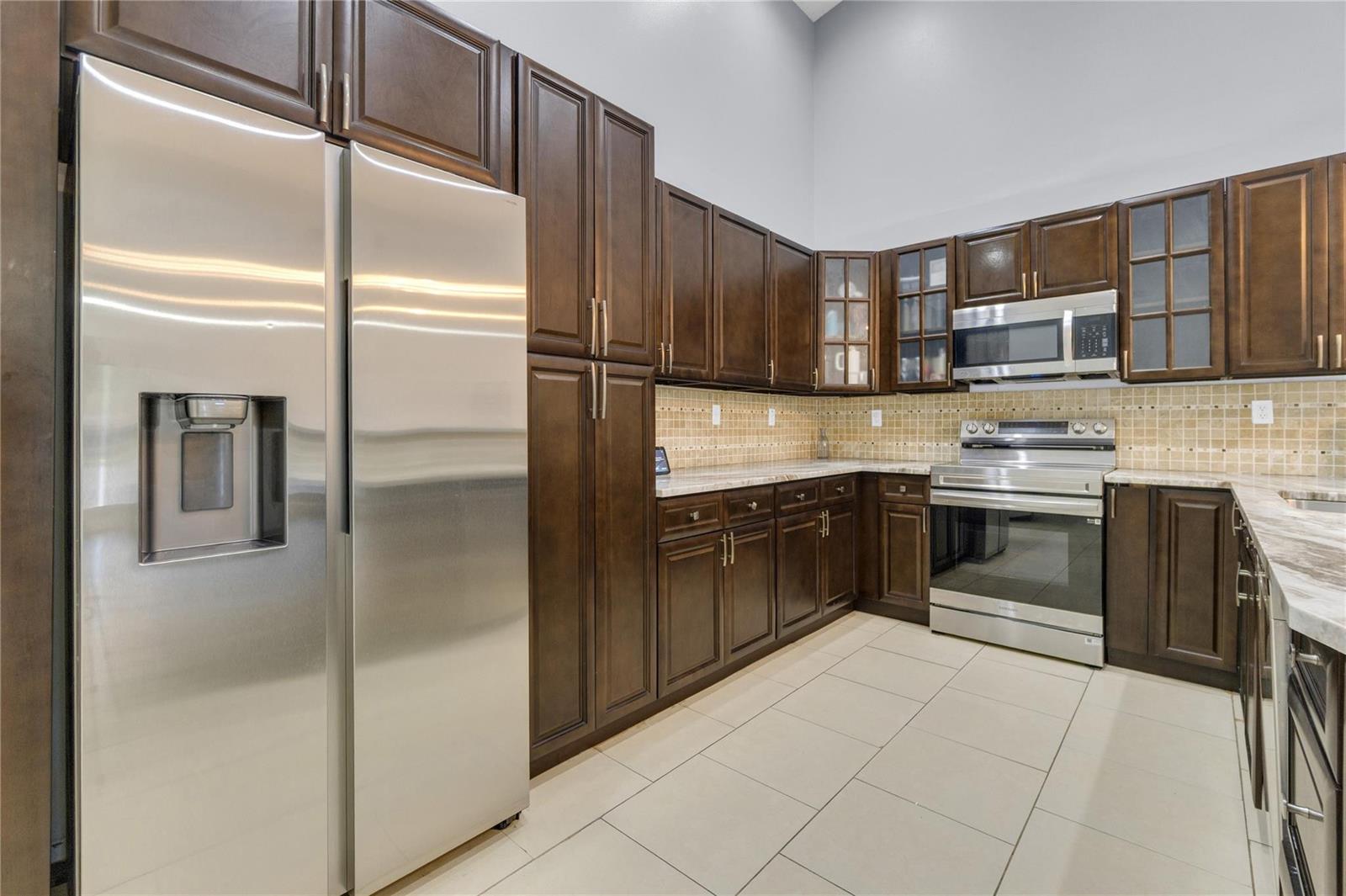 A kitchen features dark wood cabinetry, stainless steel appliances, and a tan tiled backsplash — 3003 La Mirage # 3003, Lauderhill FL 33319, LAUDERHILL, FL