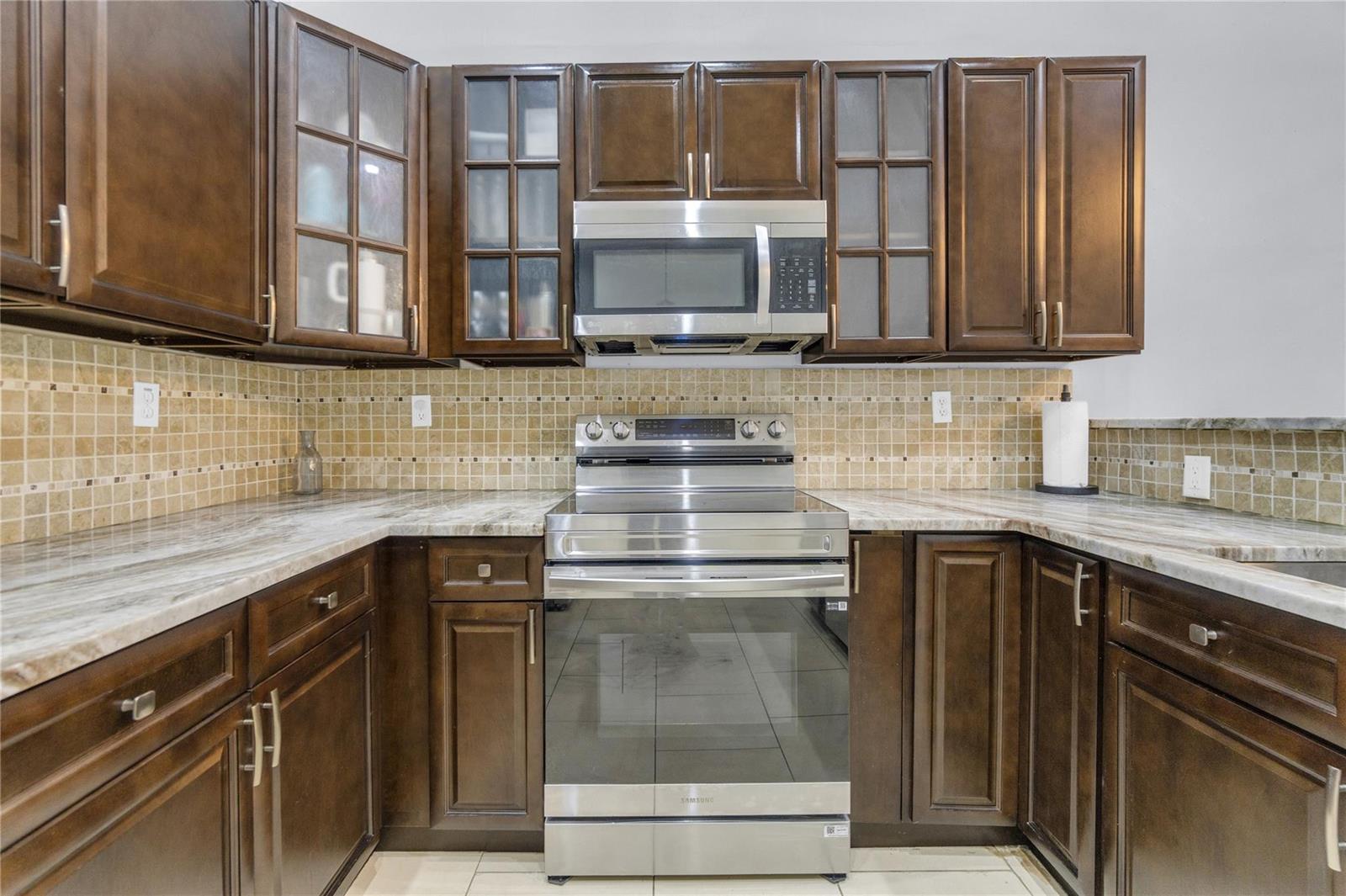 A kitchen features dark wood cabinets, stainless steel appliances, and a tan tiled backsplash — 3003 La Mirage # 3003, Lauderhill FL 33319, LAUDERHILL, FL