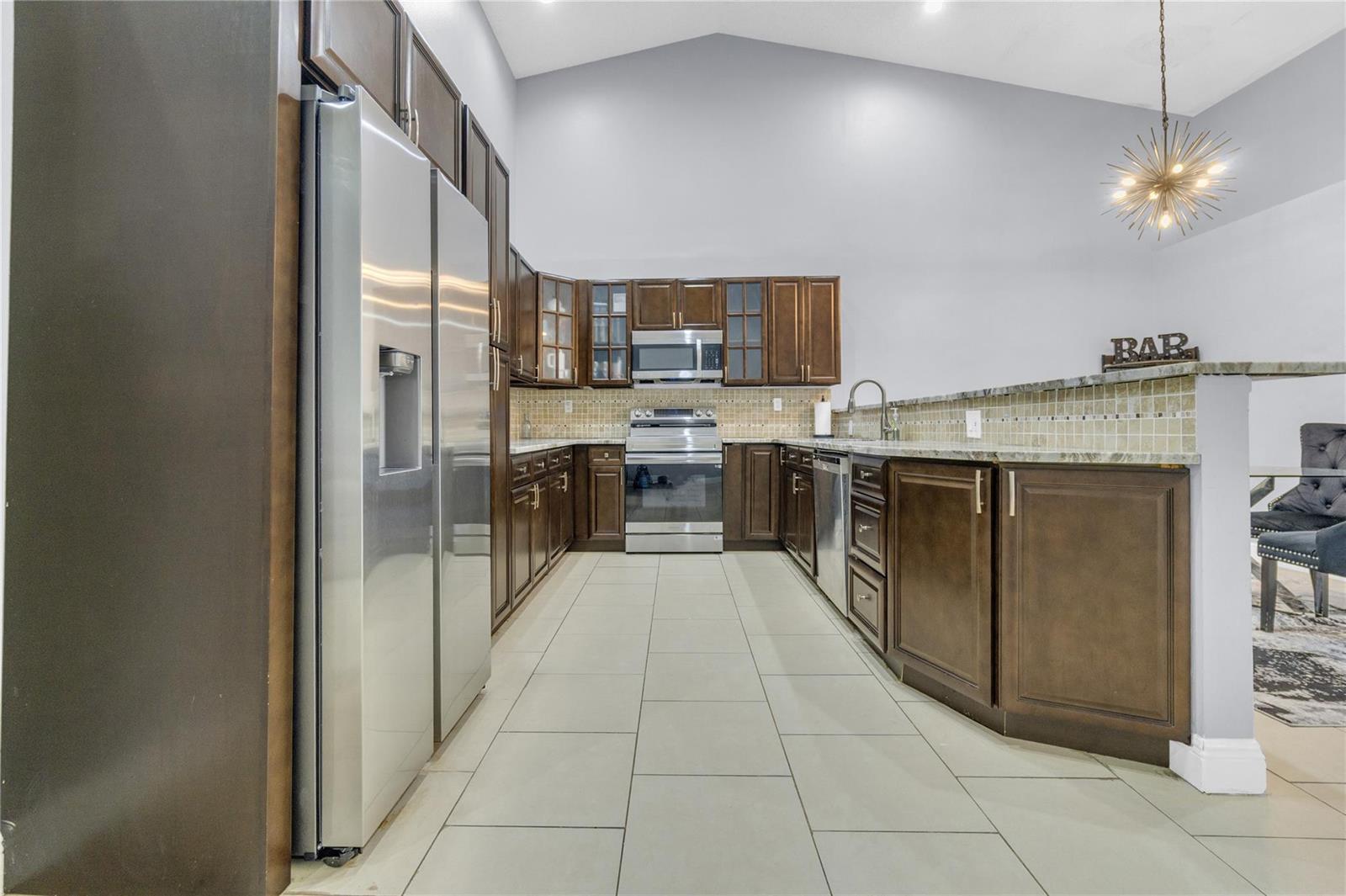A kitchen features dark wood cabinets, stainless steel appliances, tile flooring, and a vaulted ceiling — 3003 La Mirage # 3003, Lauderhill FL 33319, LAUDERHILL, FL