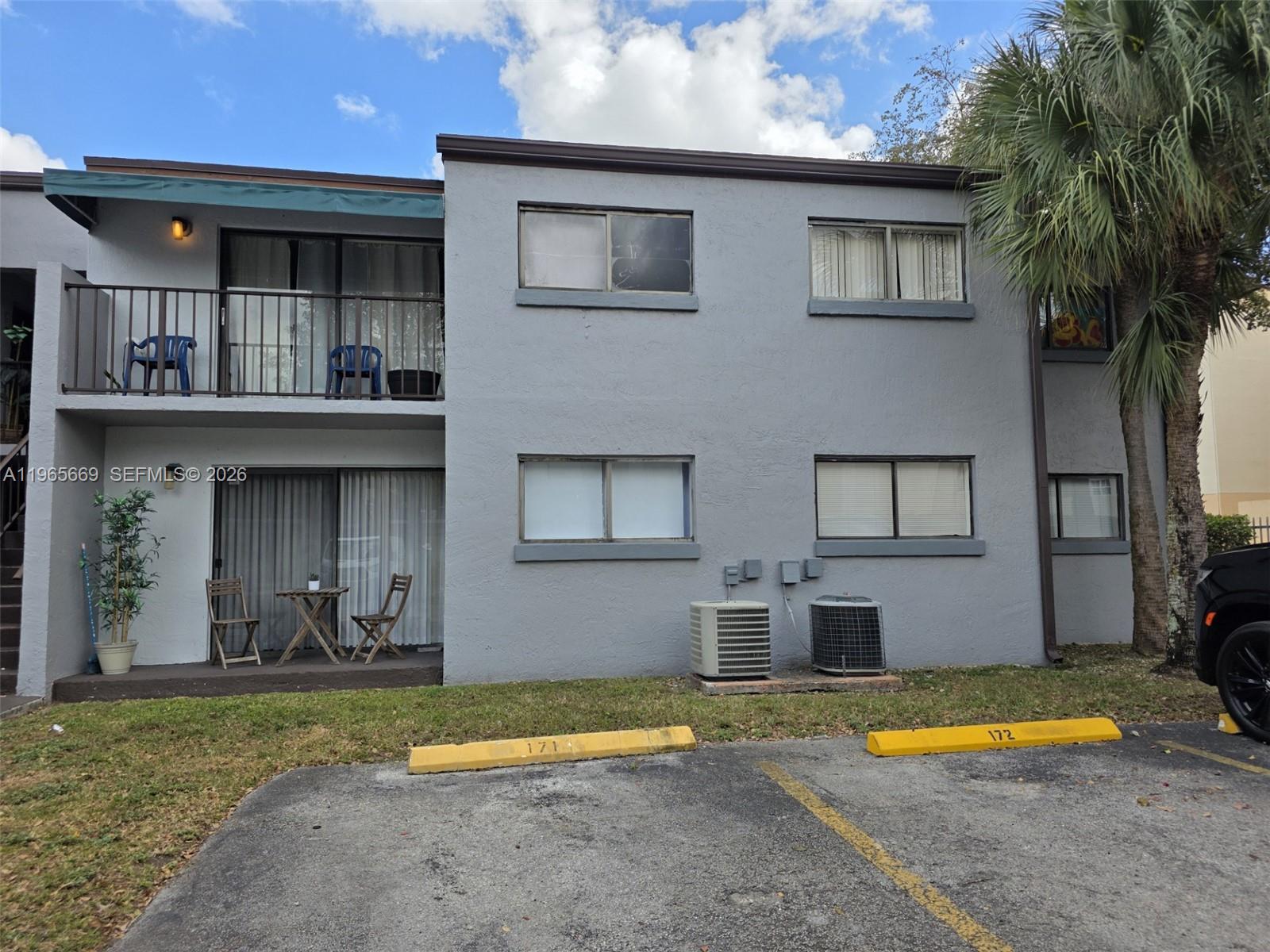 A two-story gray apartment building features balconies, patios, and assigned parking spaces — 7421 SW 152nd Ave # 101, Miami FL 33193, MIAMI, FL