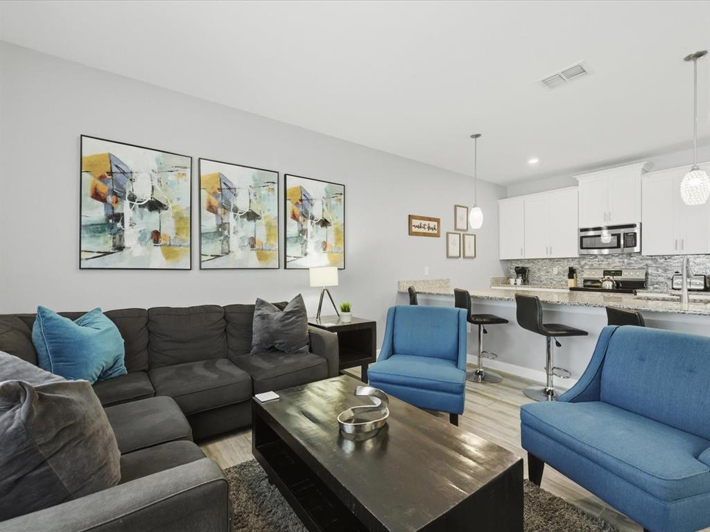 A living room with a dark sectional, two blue chairs, and an open kitchen area — 1562 MOON VALLEY DRIVE, DAVENPORT, FL