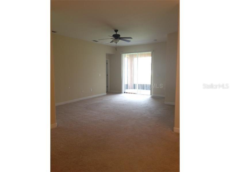 An empty living room features beige carpeting, a ceiling fan, and sliding glass patio doors — 14010 HOLLOW LEAF PLACE, RIVERVIEW, FL