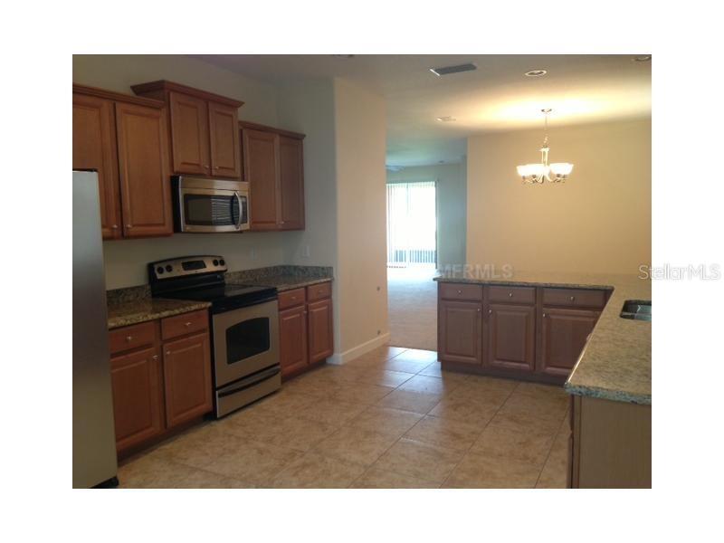 A kitchen features wood cabinets, granite countertops, stainless steel appliances, and tile flooring — 14010 HOLLOW LEAF PLACE, RIVERVIEW, FL