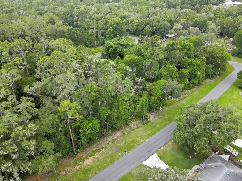 An aerial view shows a paved road bordering a densely wooded lot with a house — 1048 W MAXIMILIAN PLACE, CITRUS SPRINGS, FL