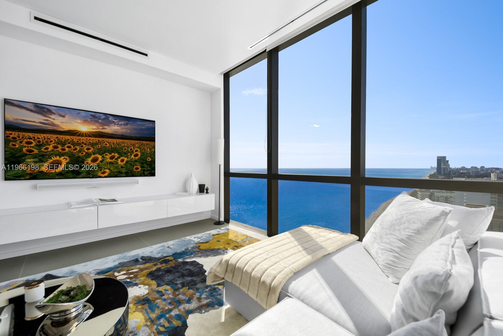 A modern living room features a white media console, patterned rug, and floor-to-ceiling ocean views — 2000 S Ocean Dr # 25B, Hallandale Beach FL 33009, HALLANDALE BEACH, FL