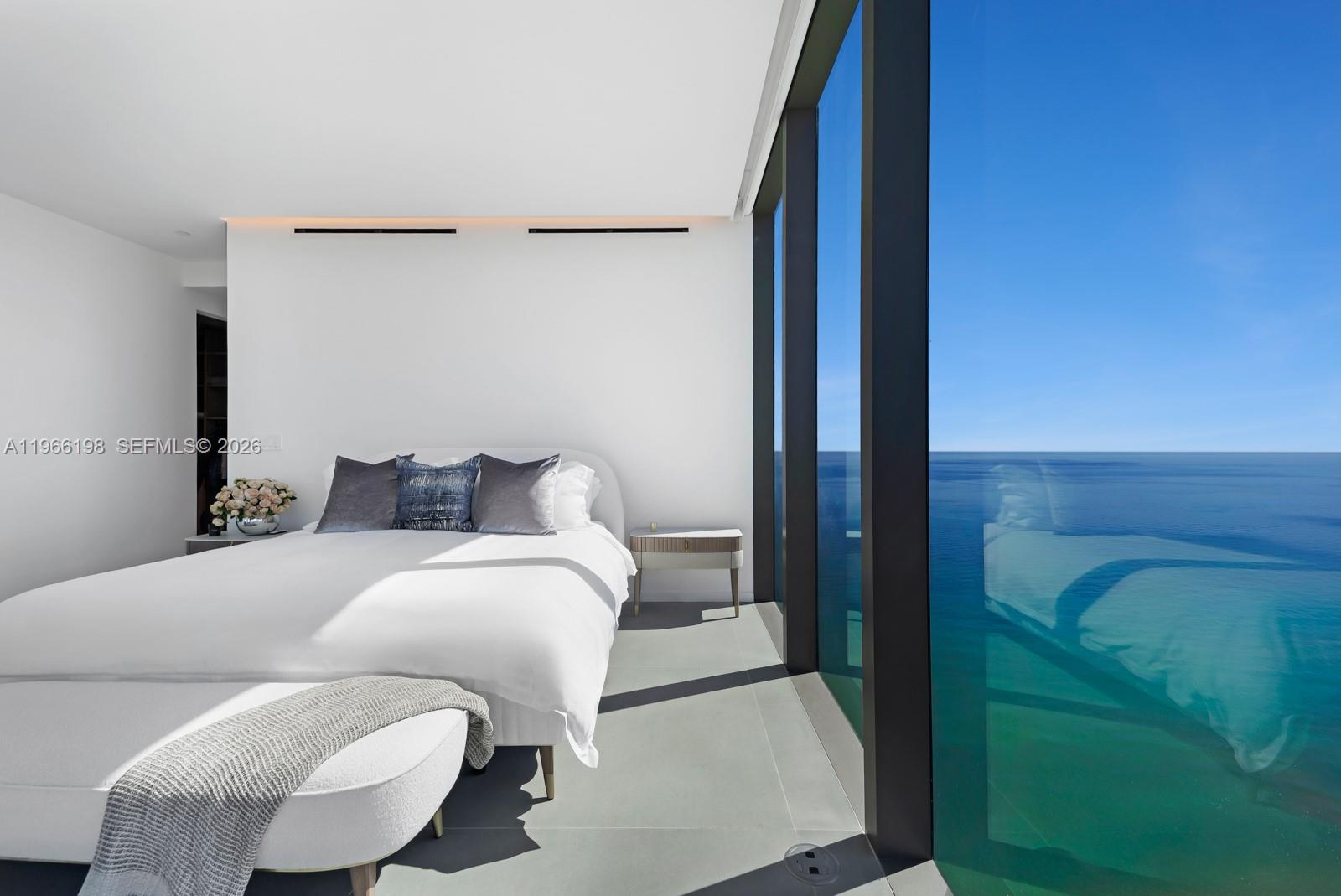 A modern bedroom features a white bed, gray flooring, and floor-to-ceiling windows overlooking the ocean — 2000 S Ocean Dr # 25B, Hallandale Beach FL 33009, HALLANDALE BEACH, FL