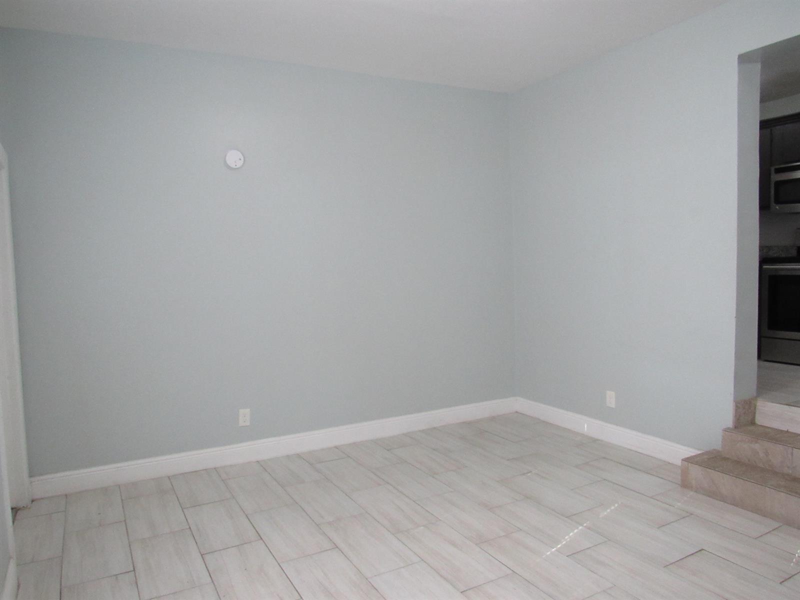An empty room with light blue walls, wood-look tile flooring, and steps leading to a kitchen — 4283 Cocoanut Road # 3, West Palm Beach FL 33406, WEST PALM BEACH, FL
