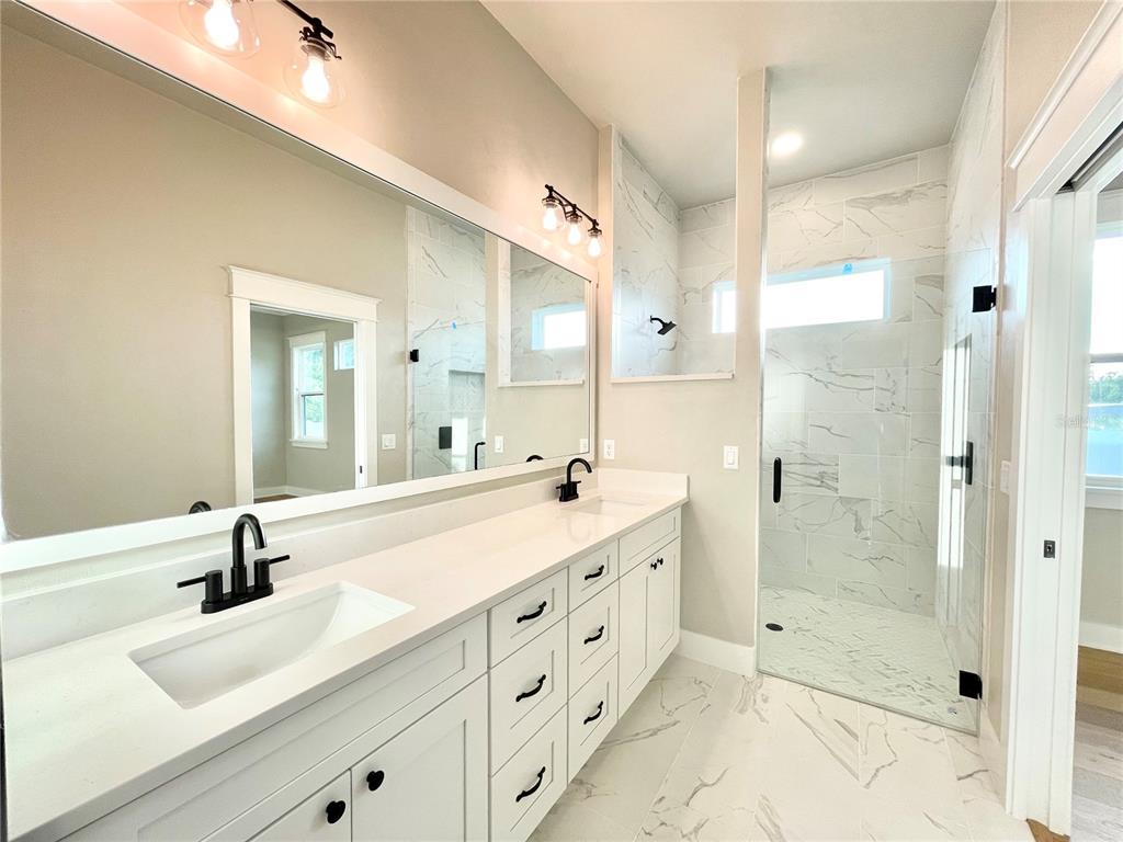 A modern bathroom features a double vanity with white cabinets, marble countertops, and a glass shower — 122 SW 212TH DRIVE, NEWBERRY, FL