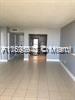 An empty room with light-colored tile flooring and gray walls leads to a kitchen area — 13499 Biscayne Blvd # 1603, North Miami FL 33181, NORTH MIAMI, FL