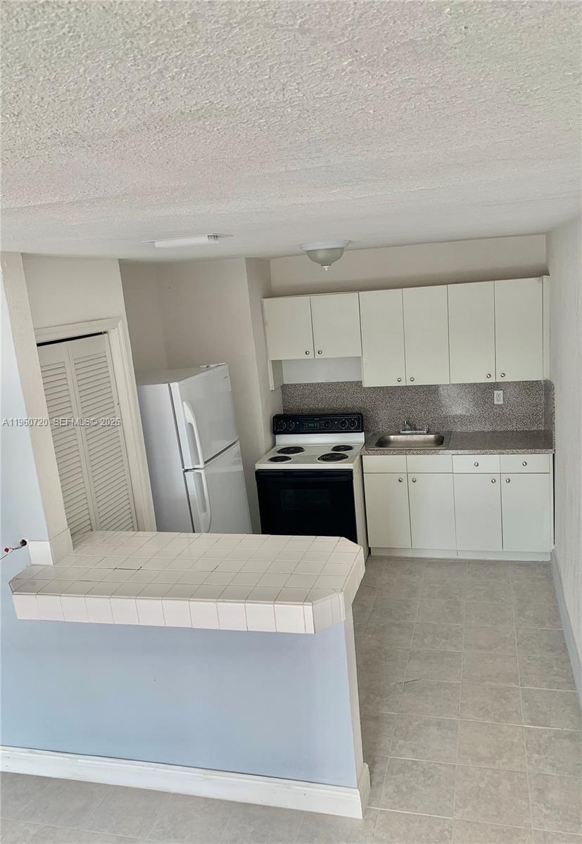 A small kitchen features white cabinets, a black stove, a white refrigerator, and a tiled counter — 22365 SW 115th Ct # 4, Miami FL 33170, MIAMI, FL