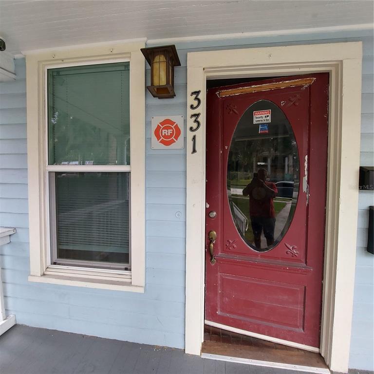 A light blue house exterior features a red front door with an oval glass window — 331 W NEW YORK AVENUE, DELAND, FL