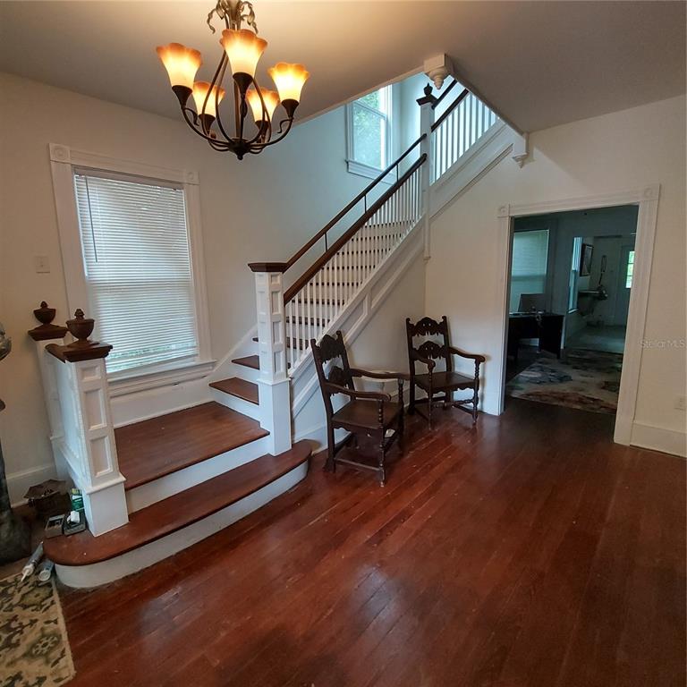A foyer features hardwood floors, a wooden staircase with white railings, and two antique chairs — 331 W NEW YORK AVENUE, DELAND, FL