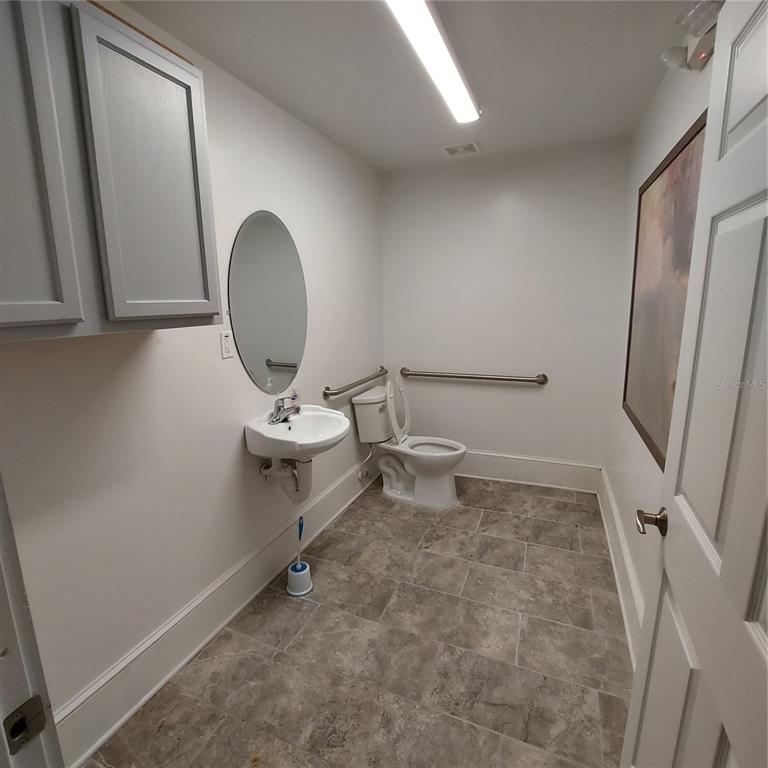 A bathroom with a wall-mounted sink, toilet, grab bars, gray cabinets, and tiled flooring — 331 W NEW YORK AVENUE, DELAND, FL