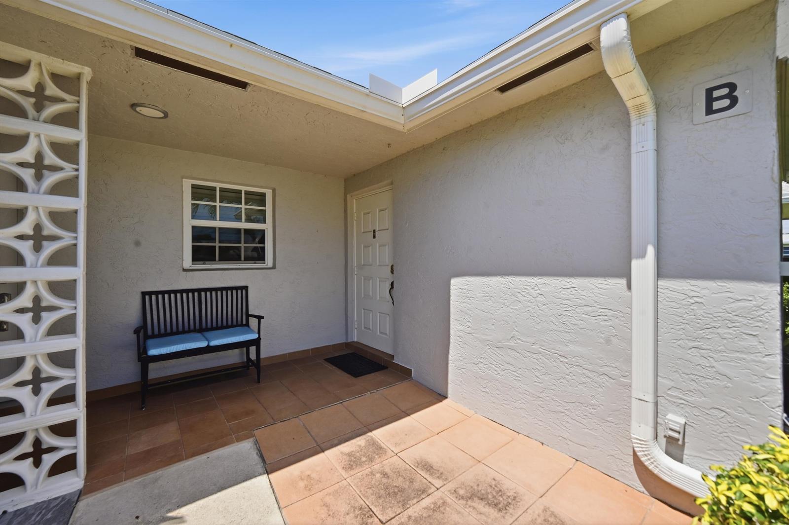 A covered entryway features a tiled patio, a black bench, and a white front door — 14589 Canalview Drive # B, Delray Beach FL 33484, DELRAY BEACH, FL