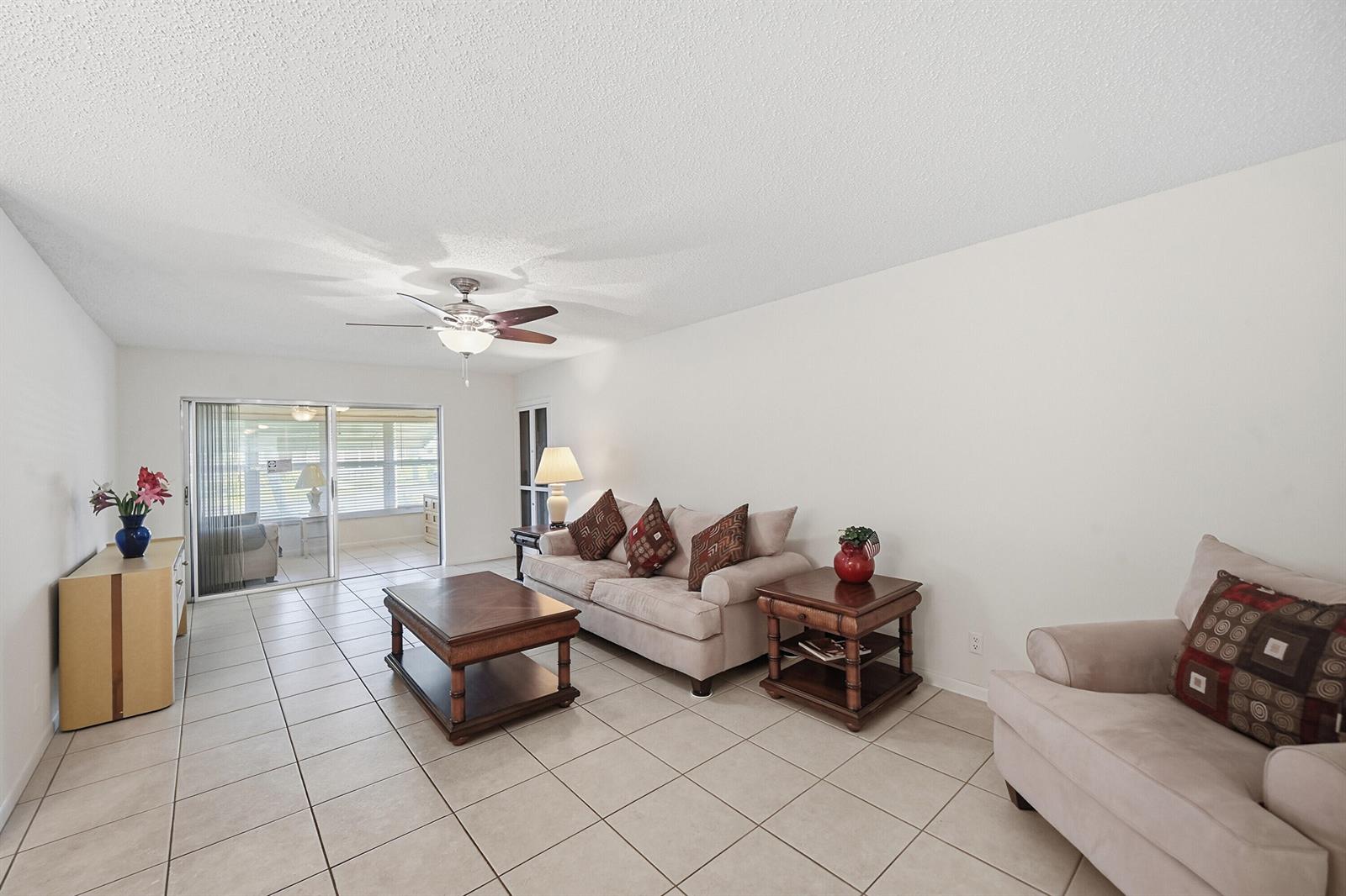 A living room with beige tile flooring, a beige sofa, a matching armchair, and a ceiling fan — 14589 Canalview Drive # B, Delray Beach FL 33484, DELRAY BEACH, FL