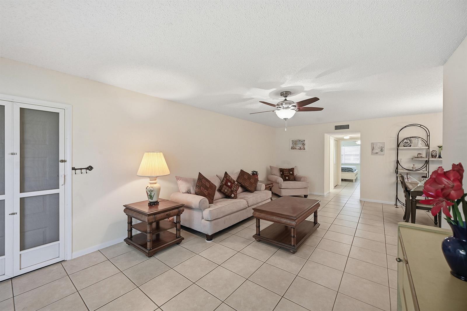A living room features beige tile flooring, a neutral sofa, a coffee table, and a ceiling fan — 14589 Canalview Drive # B, Delray Beach FL 33484, DELRAY BEACH, FL