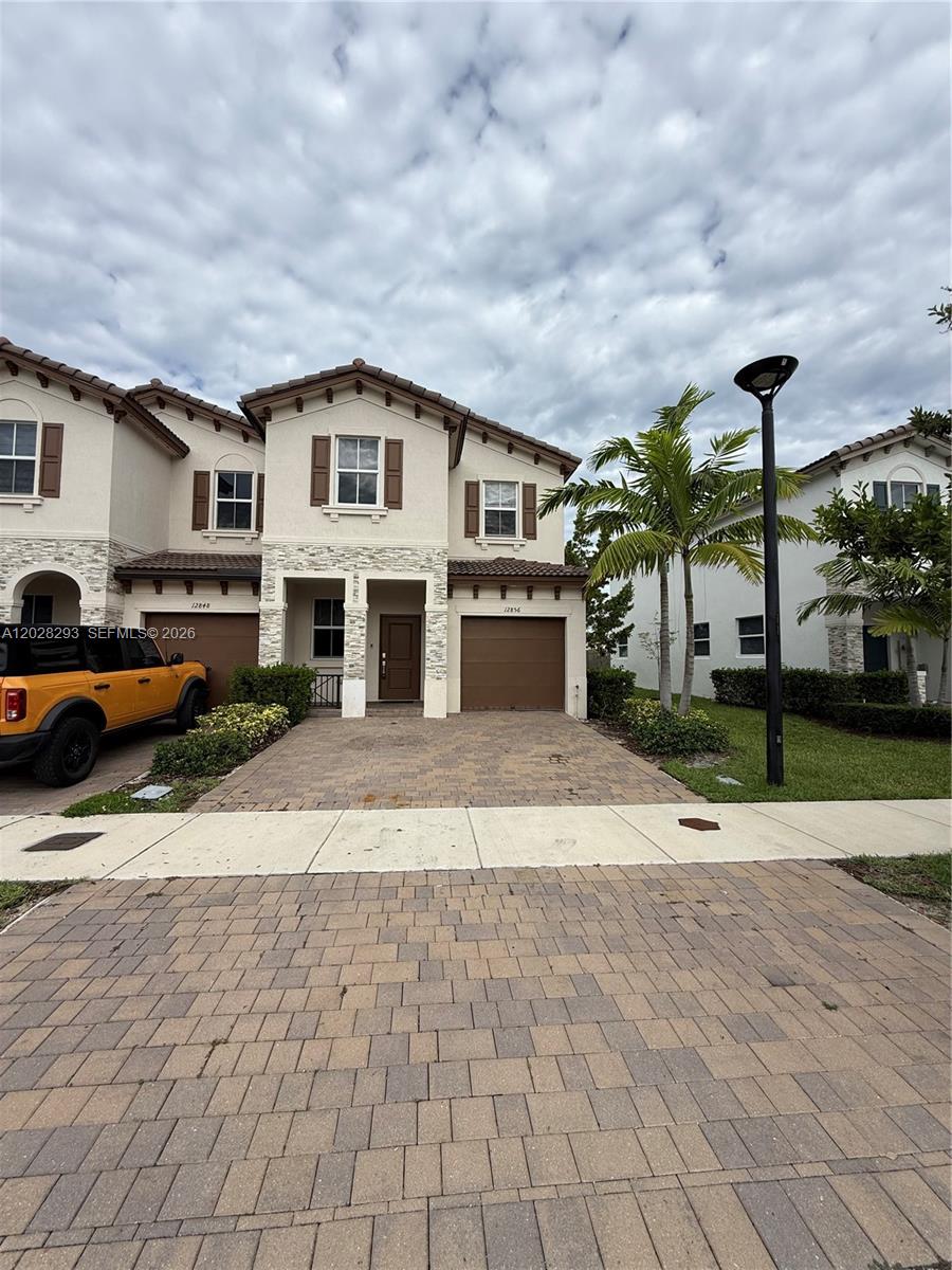 A two-story townhouse with a paved driveway, a one-car garage, and a palm tree — 12856 NW 22nd Pl # 12856, Miami FL 33167, MIAMI, FL