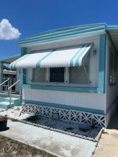 The exterior of a mobile home features white siding, teal trim, and a striped window awning — 2430 SE Penny Lane, Stuart FL 34994, STUART, FL