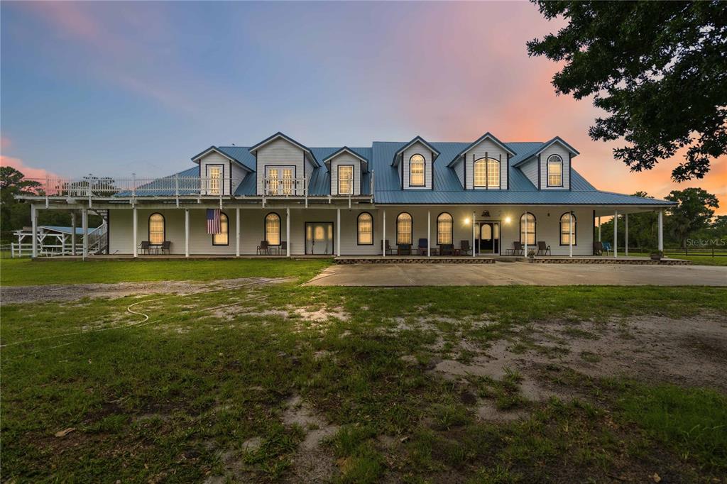 A large, two-story white farmhouse with a metal roof and a wraparound porch at sunset — 31243 BEAR POND DRIVE, SORRENTO, FL