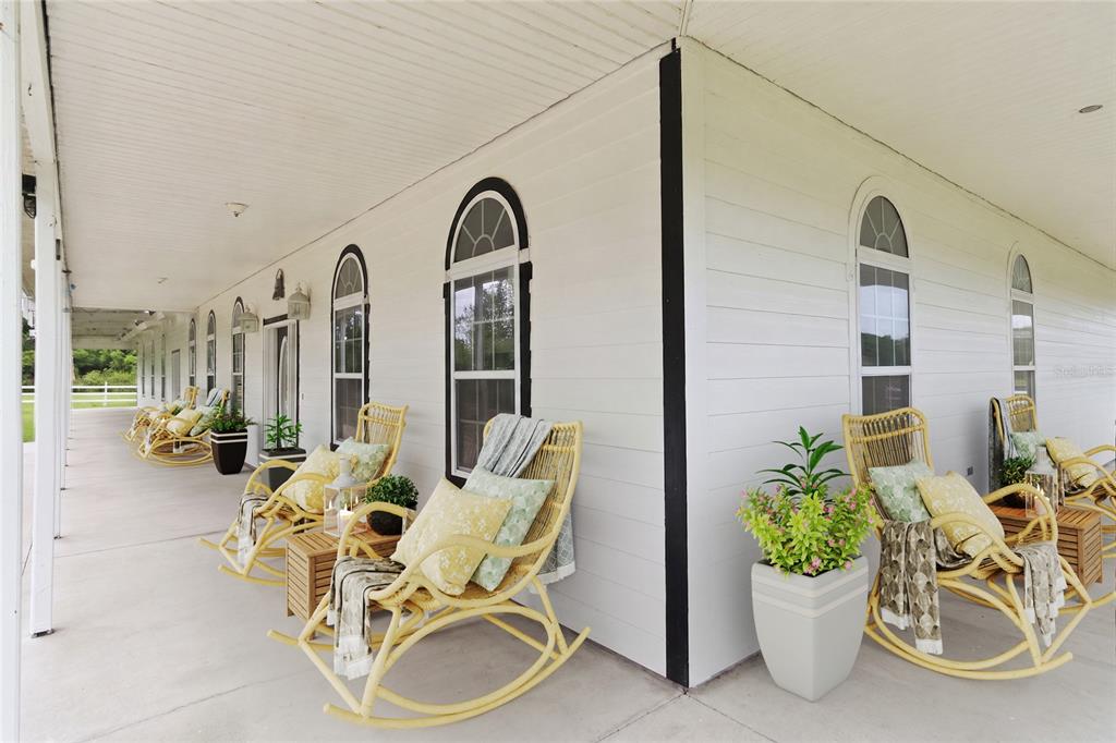 A long, covered porch features white siding, arched windows, and several yellow wicker rocking chairs — 31243 BEAR POND DRIVE, SORRENTO, FL