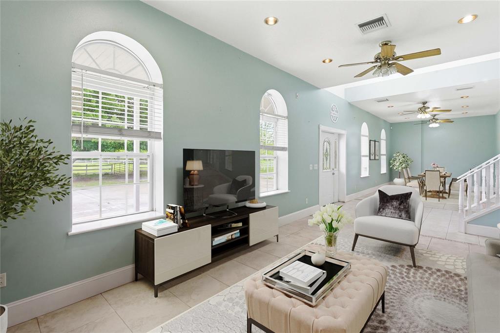 A living room with light blue walls, arched windows, tile floors, and a dining area — 31243 BEAR POND DRIVE, SORRENTO, FL