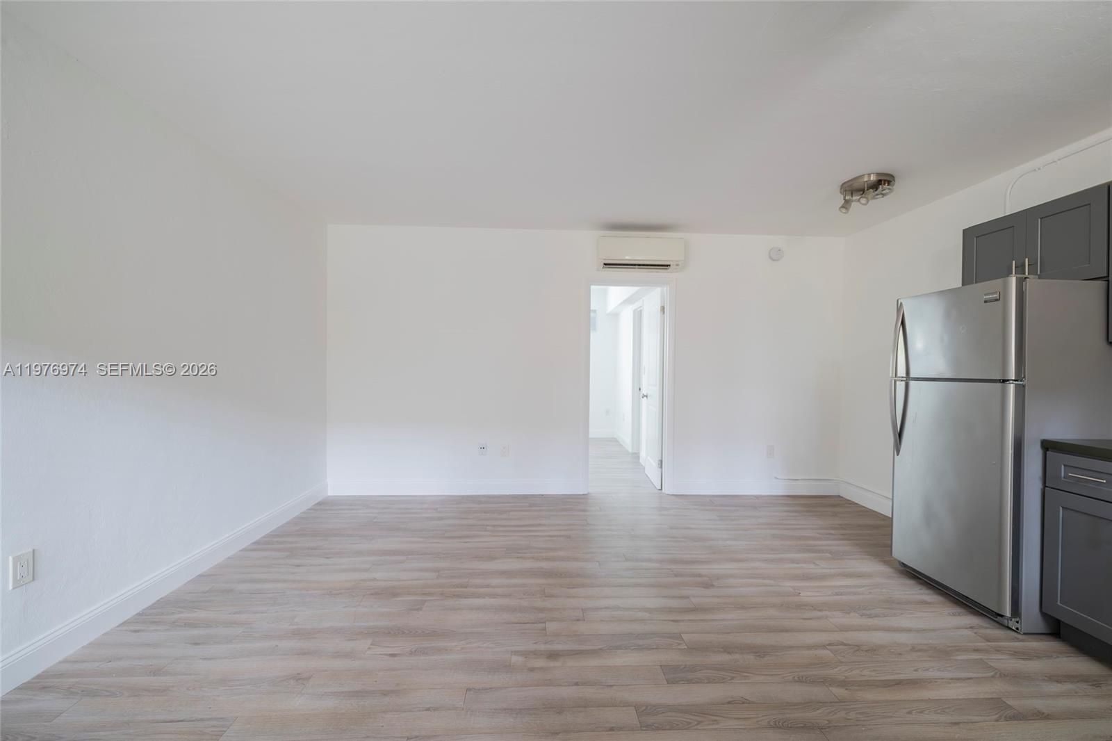 An empty room with light wood-look flooring, white walls, and a stainless steel refrigerator — 7901 SW 64th Ave # 2, South Miami FL 33143, SOUTH MIAMI, FL