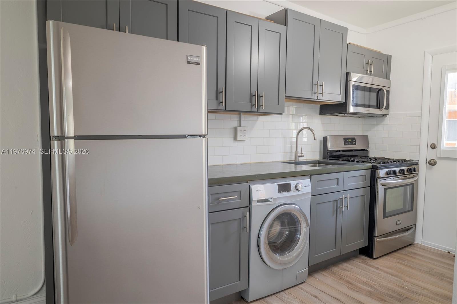 A kitchen features gray cabinets, stainless steel appliances, a built-in washer, and white subway tile — 7901 SW 64th Ave # 2, South Miami FL 33143, SOUTH MIAMI, FL