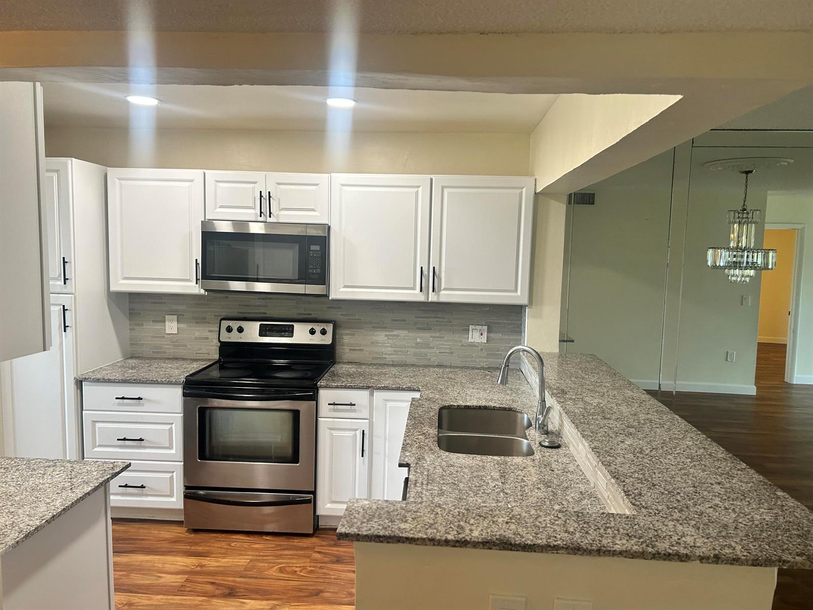 A kitchen features white cabinets, granite countertops, stainless steel appliances, and a double-basin sink — 3521 Environ Boulevard # B503, Lauderhill FL 33319, LAUDERHILL, FL
