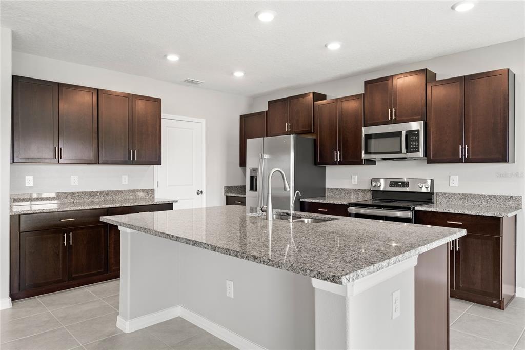 A kitchen features dark wood cabinets, granite countertops, a central island, and stainless steel appliances — 16649 CARLTON POND STREET, WIMAUMA, FL
