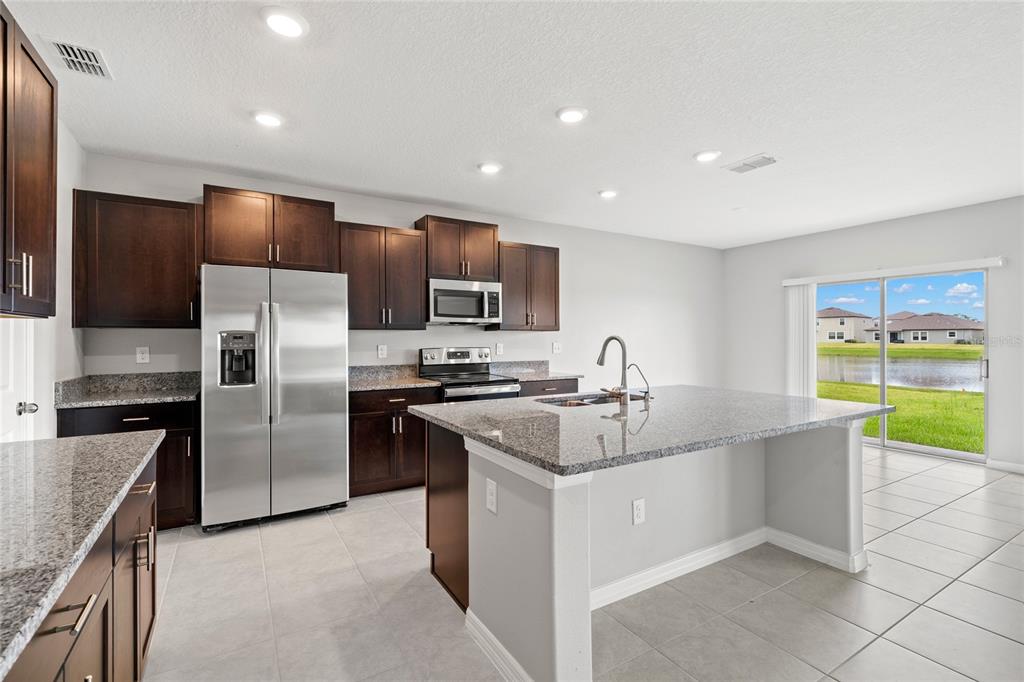 A kitchen with dark wood cabinets, granite countertops, stainless steel appliances, and a center island — 16649 CARLTON POND STREET, WIMAUMA, FL