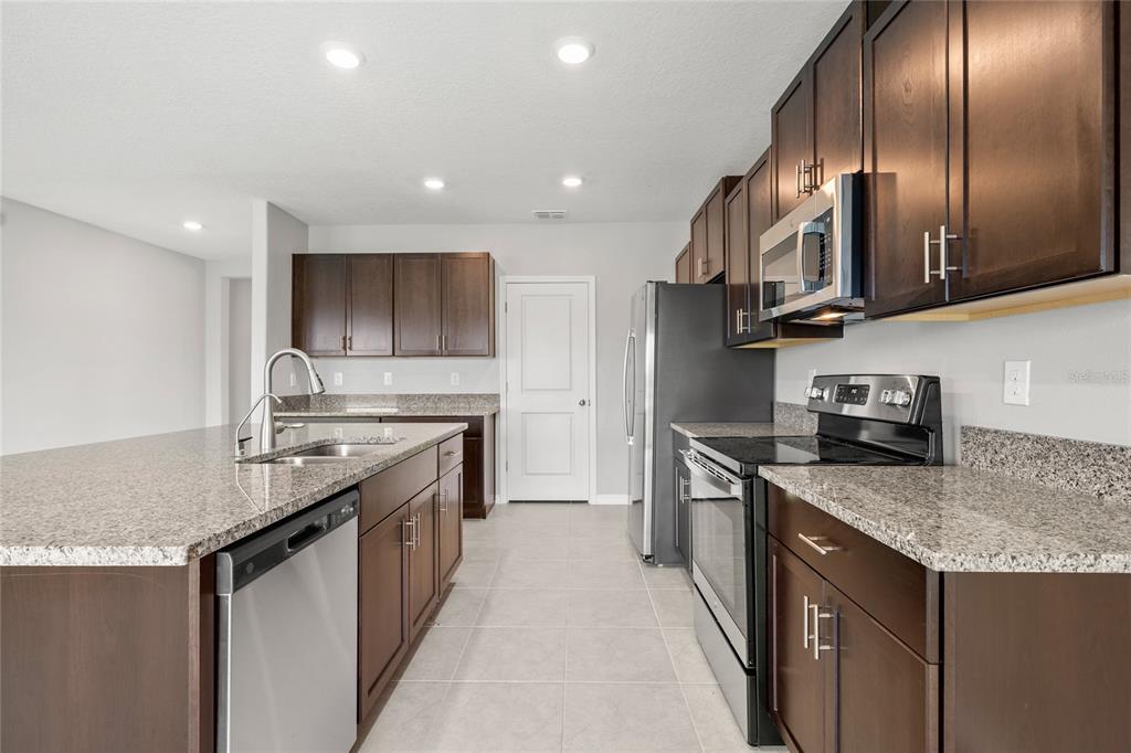 A kitchen features dark wood cabinets, granite countertops, stainless steel appliances, and tile flooring — 16649 CARLTON POND STREET, WIMAUMA, FL