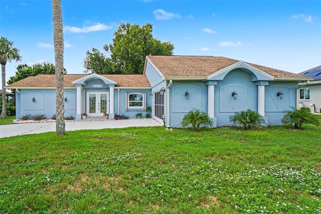 A light blue single-story house features a white double-door entrance and a large front lawn — 12001 SW KINGSWAY CIRCLE, LAKE SUZY, FL