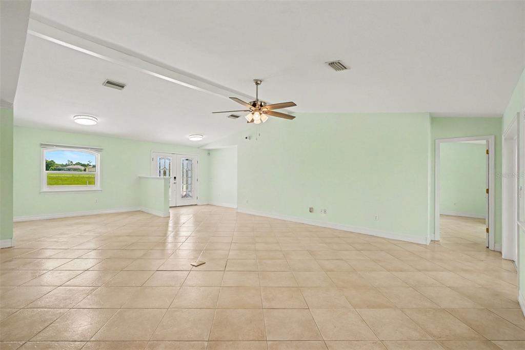 A spacious, light green living room features beige tile flooring and a ceiling fan — 12001 SW KINGSWAY CIRCLE, LAKE SUZY, FL
