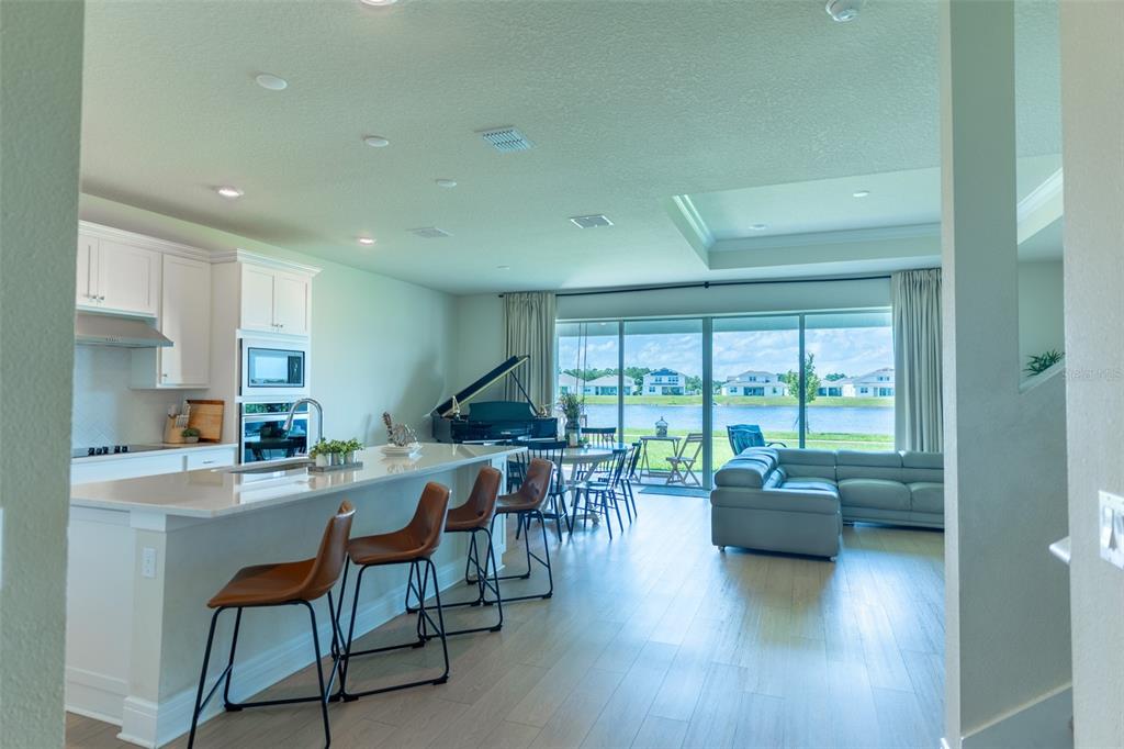 An open-concept kitchen and living area features a large island, piano, and sliding glass doors — 6067 FOREST PERCH DRIVE, ST CLOUD, FL