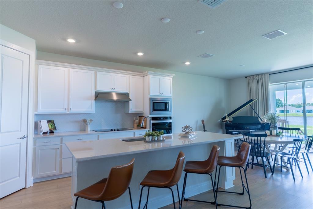 A modern kitchen features white cabinetry, a large island with bar stools, and a dining area — 6067 FOREST PERCH DRIVE, ST CLOUD, FL