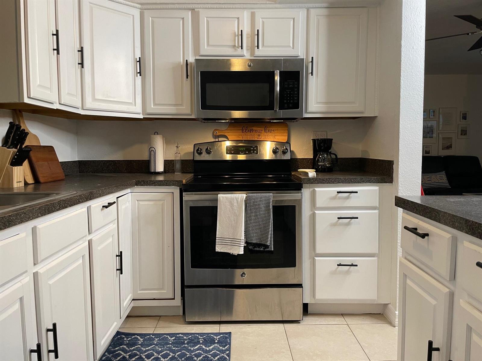 A kitchen features white cabinets, stainless steel appliances, dark countertops, and a tile floor — 1067 SW 3rd Street, Hallandale Beach FL 33009, HALLANDALE BEACH, FL